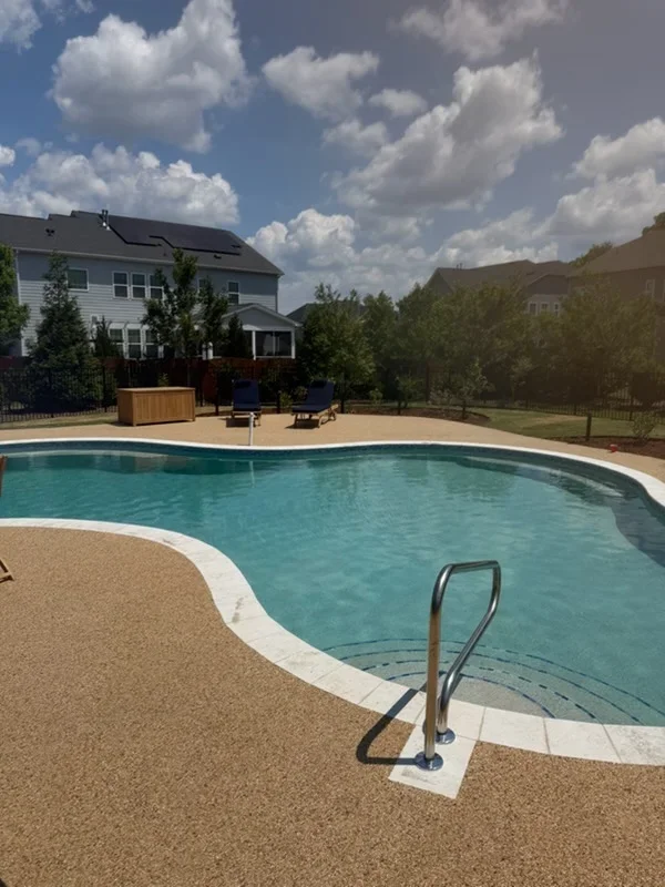 In-ground swimming pool with aggregate decking, lounge chairs, and two-story home in background