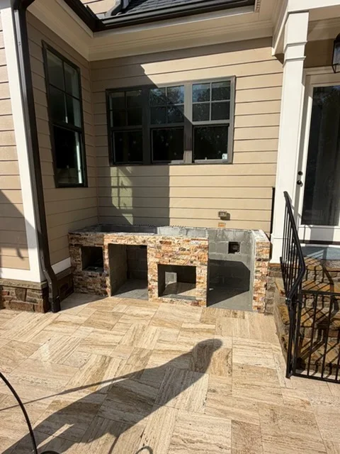 Stone outdoor kitchen with grill and herringbone paver patio under covered structure