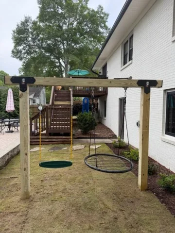 Wooden pergola with swing set and sandbox in sandy backyard play area