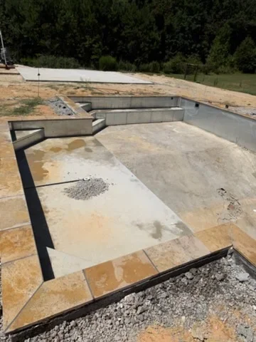 In-ground concrete pool with travertine tile decking and black steel coping during construction