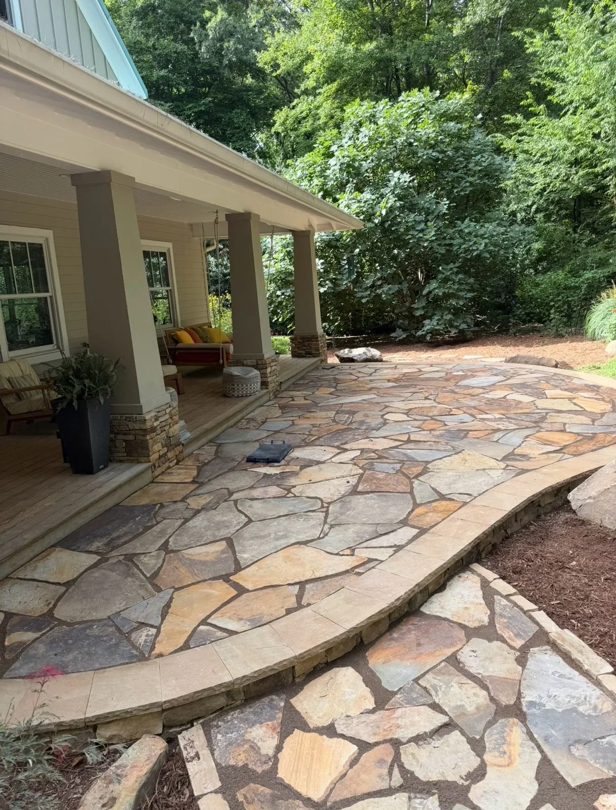 Irregular flagstone patio with mortar joints and curved stone border edge adjacent to covered porch