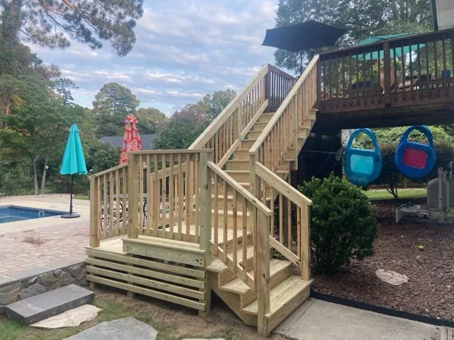 Elevated wooden deck with composite stairs, railings, and landing platform overlooking backyard