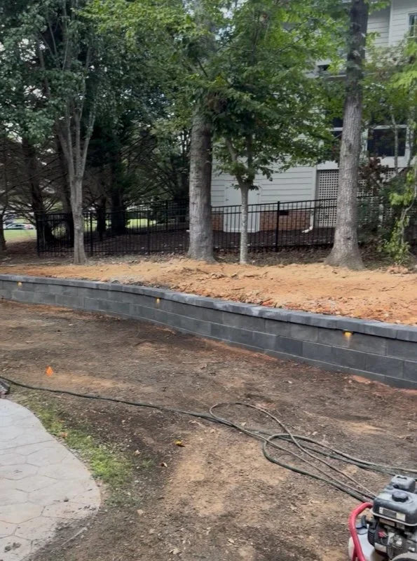 Stacked timber retaining wall with fresh mulch and graded landscape bed under mature trees