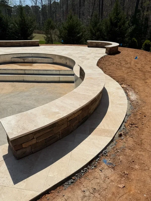 Curved concrete pool deck with stone-faced seating walls and integrated bench areas