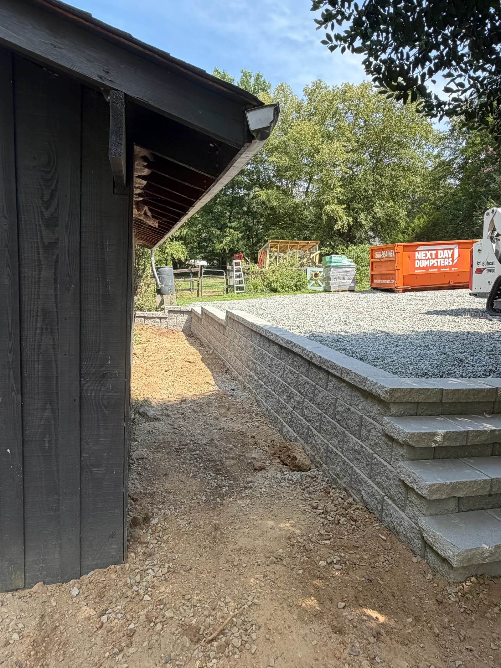 Concrete retaining wall with steps and gravel patio base next to black covered structure
