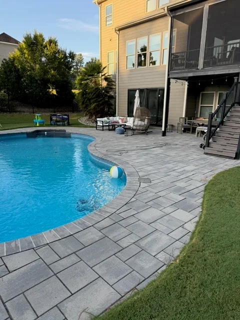 In-ground pool with gray concrete paver deck and composite deck stairs
