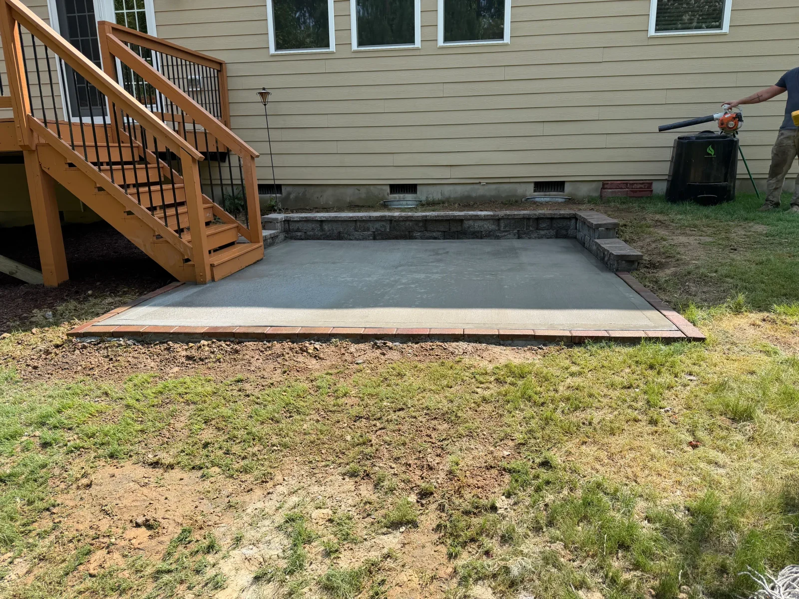 Finished concrete patio with brick border and stone retaining wall beside wooden deck