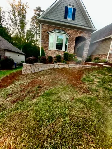 Front yard with new sod, graded beds, and stacked stone retaining wall along brick home