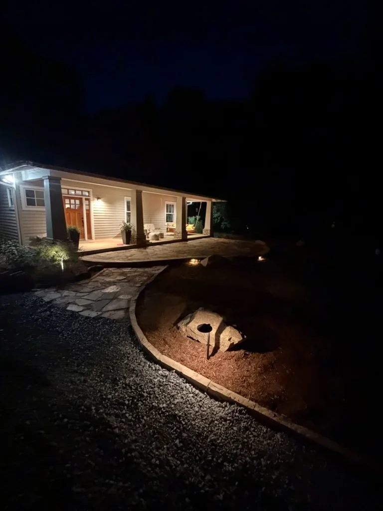 Illuminated backyard with curved stone retaining wall, gravel pathways, and landscape lighting at night